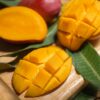Close-up of ripe mango slices on a wooden board with leaves. Perfect for tropical fruit themes.